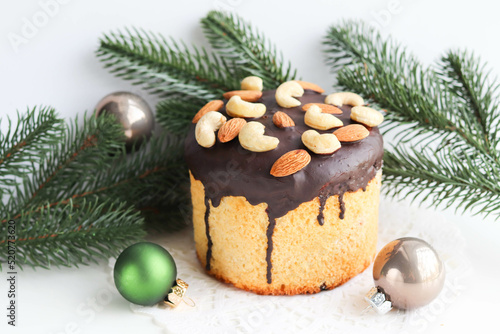 Christmas panettone with chocolate icing and nuts on the table among fir branches and Christmas decorations