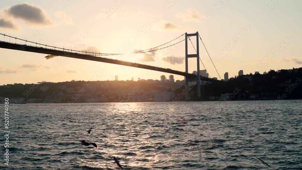 The Bosphorus Bridge in Istanbul filmed from a boat on the bosphorus strait in summer 2022 with sea birds flying around the water and the sun setting moving behind the bridge traffic cars passing 4k The Bosphorus Bridge in Istanbul filmed from a boat on the bosphorus strait in summer 2022 with sea birds flying around the water and the sun setting moving behind the bridge traffic cars passing 4k