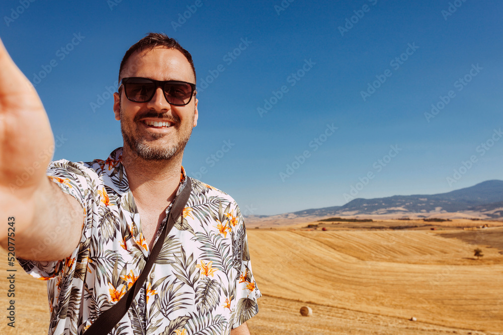 Europe luxury travel vacation tourist in Tuscany, Italy. Vacation cheerful man taking selfie photo with phone at field. Summer holiday destination. Europe luxury travel vacation tourist in Tuscany, Italy. Vacation cheerful man taking selfie photo with phone at field. Summer holiday destination.