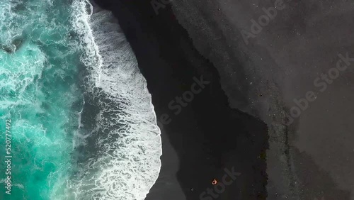 Blaues Meer und schwarzer Strand mit der Drohne gefilmt. Ein Pärchen läuft am schwarzen Strand entlang. Vogelperspektive am Strand. 1 photo