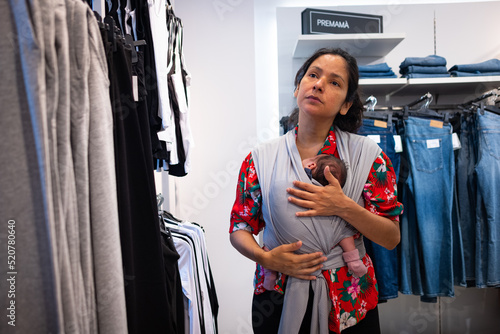 Photos A mother carrying a newborn child in babywearing fashion is seen shopping inside an apparel and clothing shop in the city downtown in Passeig de Gracia street in Barcelona, Spain on 27 July, 2022