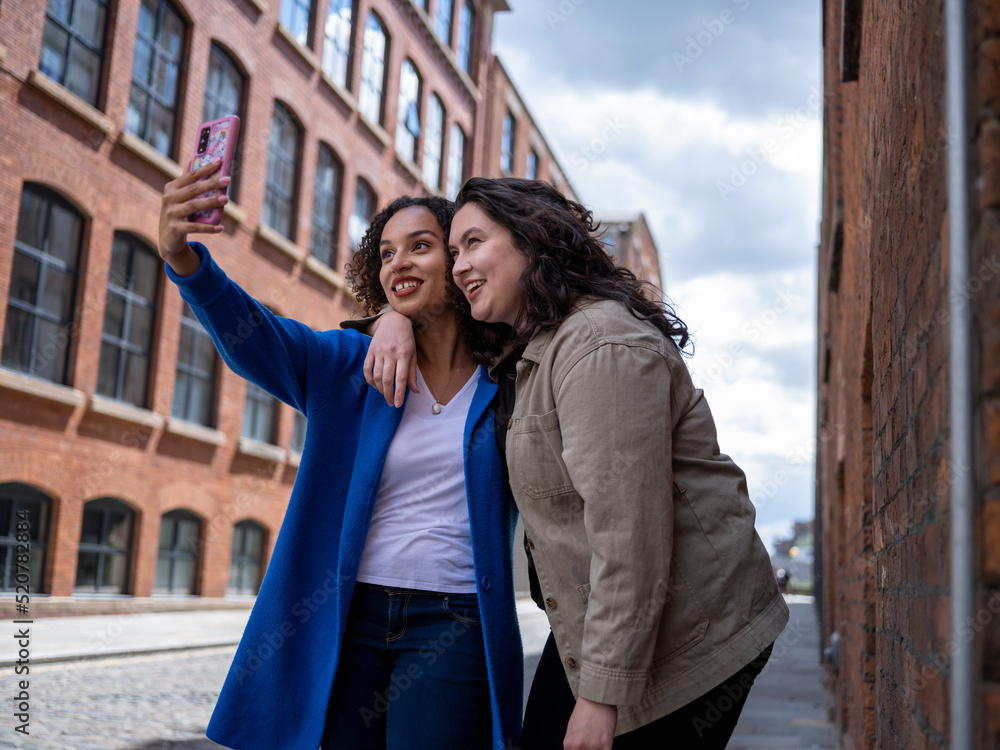 UK, Smiling lesbian couple taking selfie on street