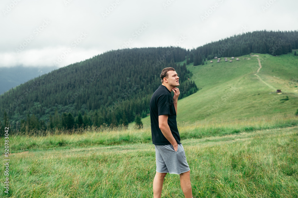 Photo of a male tourist in the mountains on the background of a beautiful view with a pasture, looking to the side. Photo of a male tourist in the mountains on the background of a beautiful view with a pasture, looking to the side.