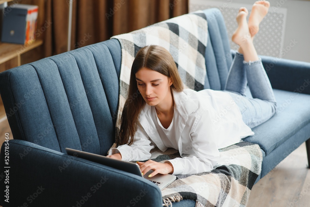 Obraz premium Freelancer working on laptop at home laying on comfortable beige sofa.