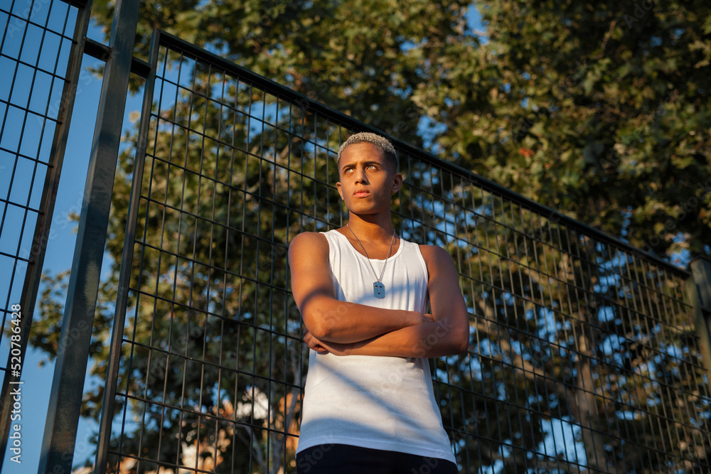 Serious black sportsman near fence on playground