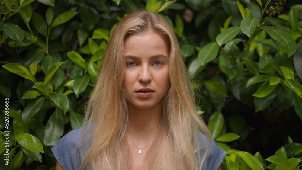 Young blonde woman looking at camera in forest, close-up Young blonde woman looking at camera in forest, close-up