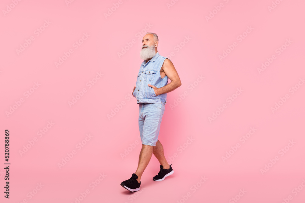 Full length photo of cute cool man pensioner dressed denim vest walking looking empty space isolated pink color background Full length photo of cute cool man pensioner dressed denim vest walking looking empty space isolated pink color background