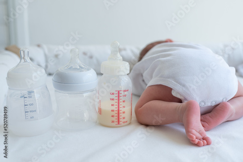 Baby's little butt with bend up legs and three bottles for milk on white blanket. Newborn - happiness for family. Concept of choice milk formula and food for kid. Back view