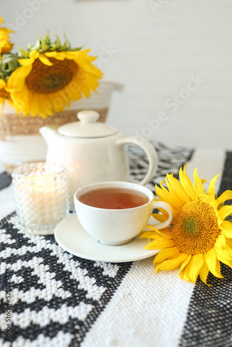 A cup of tea and a teapot with a candle on a table with sunflowers, tea time, aesthetics
