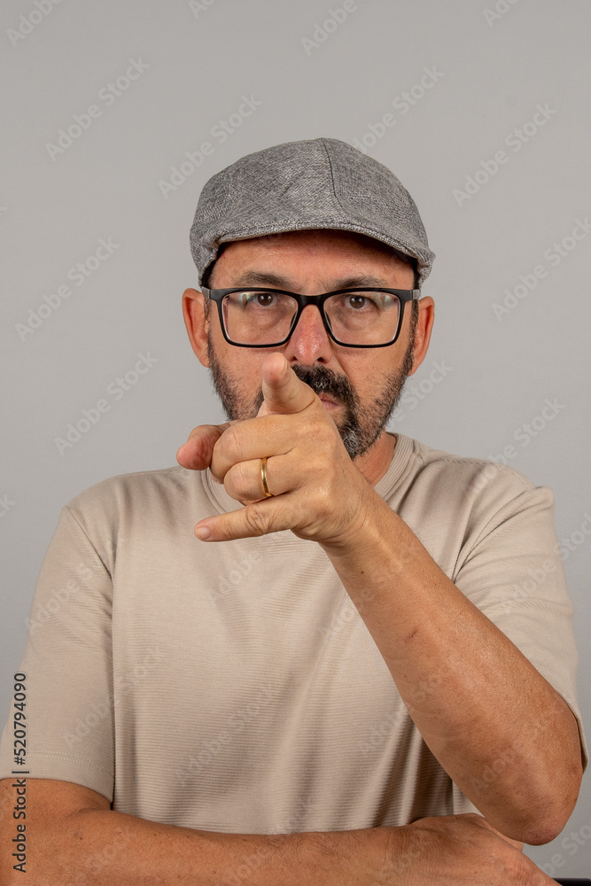Portrait of mature businessman wearing eyeglasses over gray background. Senior brazilian man 60 years old pointing at camera isolated. Portrait of mature businessman wearing eyeglasses over gray background. Senior brazilian man 60 years old pointing at camera isolated.