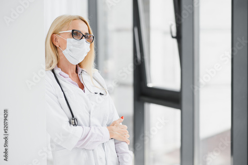 Portrait of female doctor wearing face mask for prevention while standing by the window.