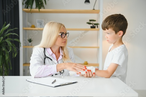 Pediatrician doctor bandaging child's arm. Broken arm in a boy.