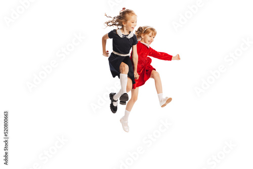 Portrait of two cheerful girls, children jumping over puddle, running isolated over white studio background. Playful