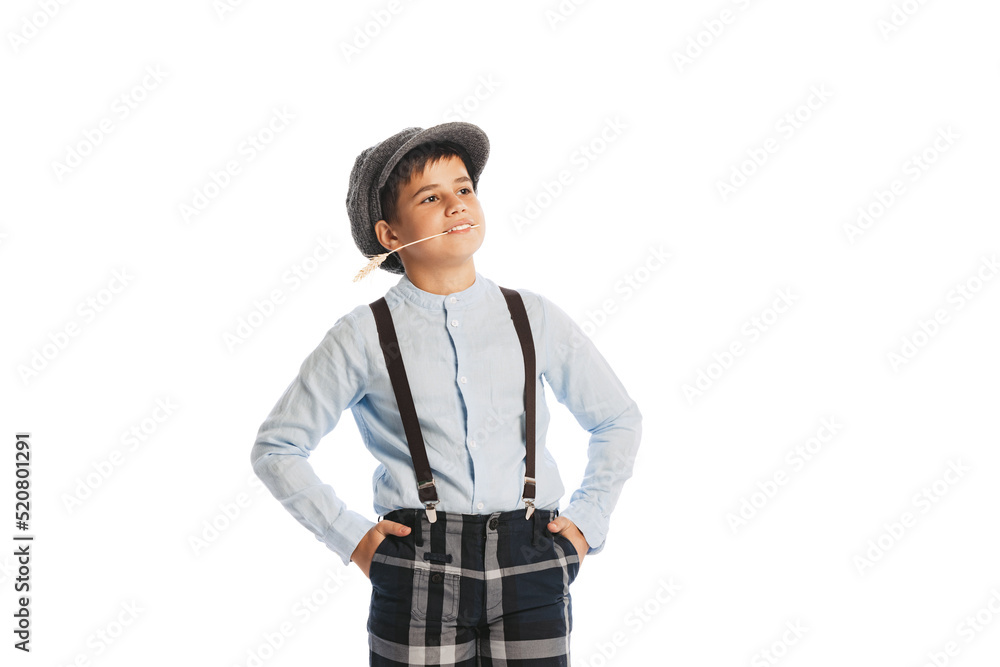 Portrait of stylish kid, boy in shirt, cap, suspenders and plaid pants smiling, posing isolated over white studio background