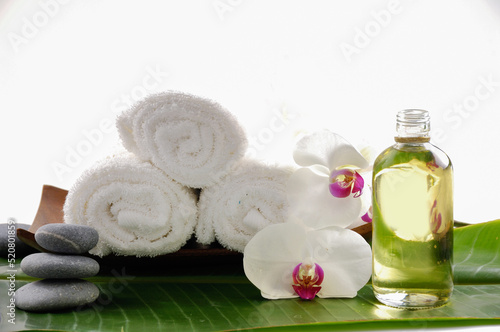 Spa setting with, three rolled towel with orchid ,oil bottle with, stacked stones leaves on big leaf background