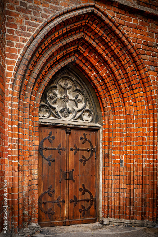 An arched doorway to a gothic style red brick cathedral.
