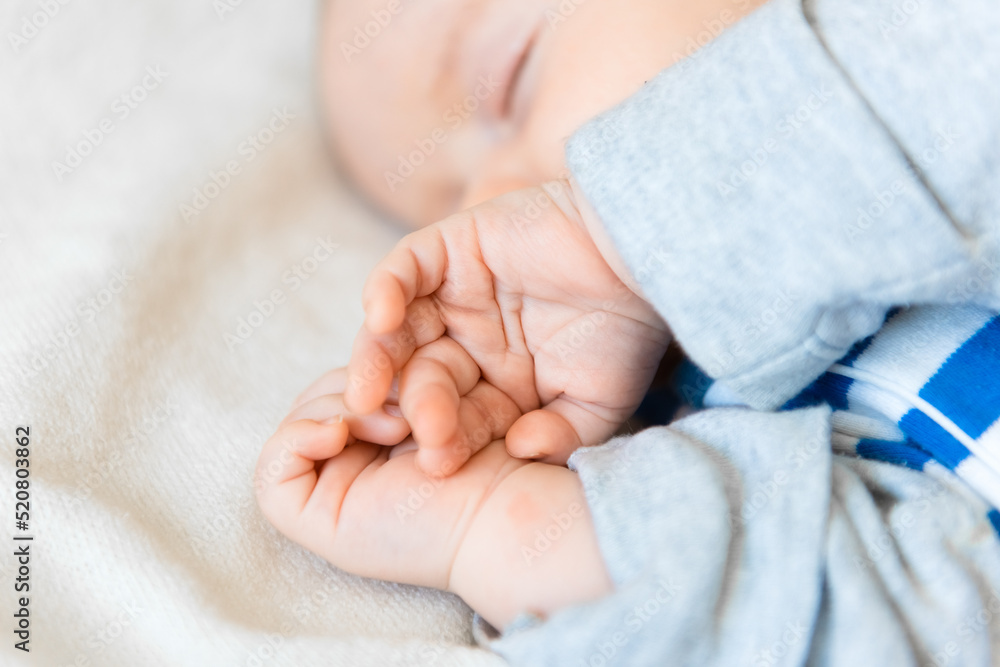Newborn Baby Sleeping. Cute Infant Child in Wrap Bodysuit. New Born Little Boy smile in Blue Clothes lying on Blanket. Small Kid Face Close up Portrait holding Hands First Newborn Baby Sleeping. Cute Infant Child in Wrap Bodysuit. New Born Little Boy smile in Blue Clothes lying on Blanket. Small Kid Face Close up Portrait holding Hands First