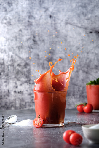 tomato juice, pour tomato juice into a glass, splashes of tomato juice, on a gray background, space for text, cherry tomatoes and salt 