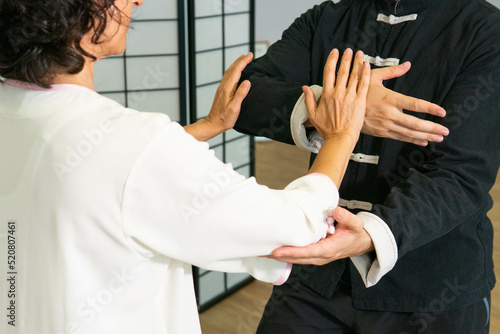 Woman pushing hands to tai chi male student indoors with black and white suits
