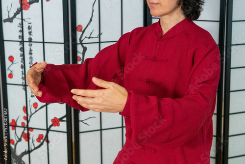 Qigong coach doing embrace gesture indoors with asian patterned folding screen in the background