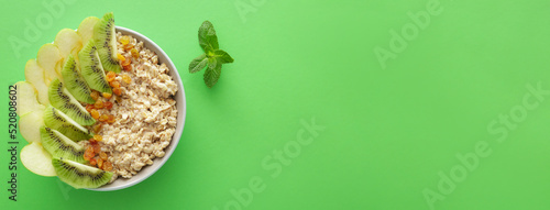 Bowl of tasty sweet oatmeal with fruits on green background with space for text, top view