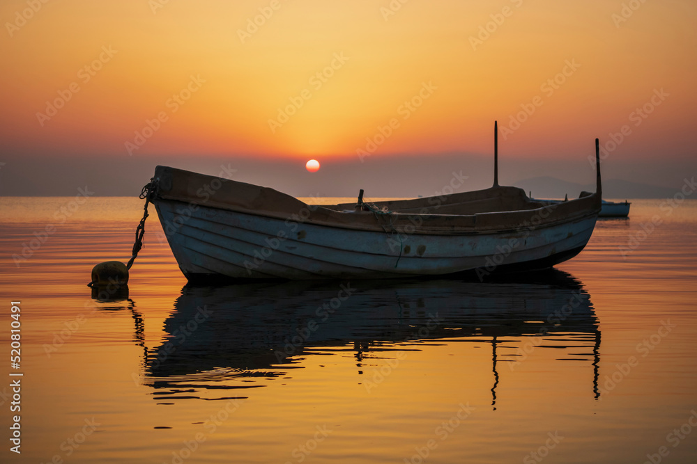 Horizontal photograph of a sunrise in the Mar Menor of Murcia, Spain, with a fishing boat in the foreground and an orange and yellow sky that is reflected in the calm waters of the sea