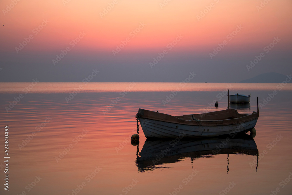 Horizontal photograph of a sunrise in the Mar Menor of Murcia, Spain, with fishing boats in the foreground and a pink sky that is reflected in the calm waters of the sea