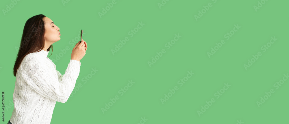 Woman kissing screen of mobile phone on green background with space for text Woman kissing screen of mobile phone on green background with space for text