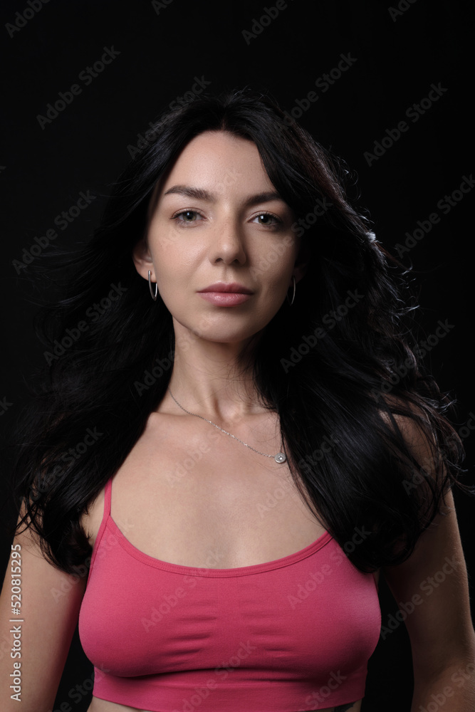 A smiling young woman model in a pink tank top in the studio. Posing on a black background. Portrait A smiling young woman model in a pink tank top in the studio. Posing on a black background. Portrait