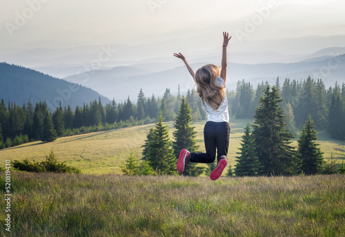 Happy little girl jumping and enjoying life at a spring meadow on the background of a picturesque mountain slopes
