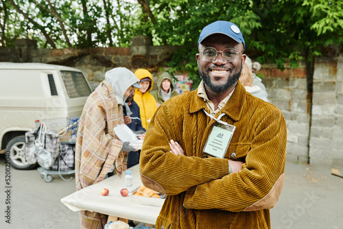 Portrait of African volunteer standing outdoors with his arms crossed and smiling at camera, he helping homeless people photo