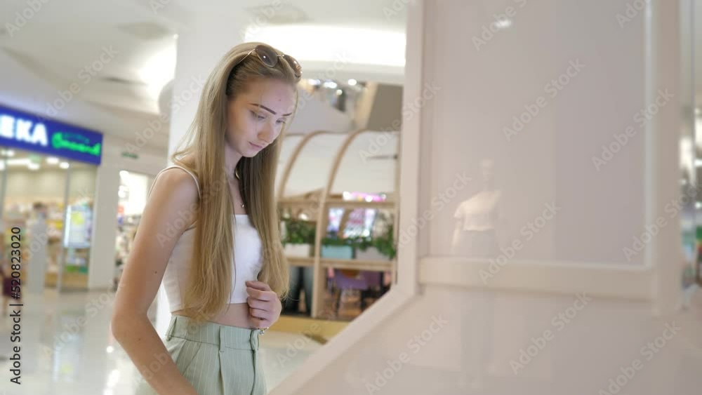 A beautiful young girl using a touch terminal in a shopping mall.The girl uses a touch terminal to search for the right store.The concept of people and technologies. Airport, online booking. Router A beautiful young girl using a touch terminal in a shopping mall.The girl uses a touch terminal to search for the right store.The concept of people and technologies. Airport, online booking. Router