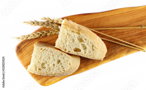 Bread slices with wheat ears on cutting board isolated on white