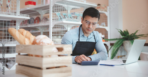 Entrepreneur male business owner in eyeglasses using computer laptop working in grocery shop store