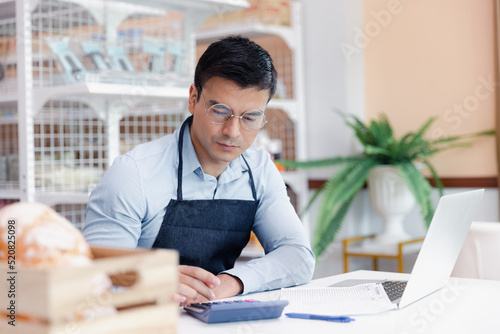 Entrepreneur male business owner in eyeglasses using computer laptop working in grocery shop store