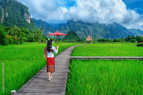 Young woman walking on wooden path with green rice field in Vang Vieng, Laos.