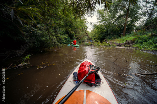 View from the first person. A trip on a SAP board. A narrow river in the middle of the forest, an extreme route. bag with water protection. Tours and tourism, active recreation.