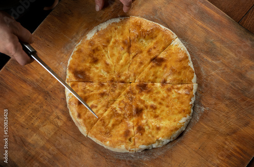 Person cutting  homemade meat pie on wooden background. Bulgarian banitsa, Georgian khachapuri, Greek tiropita