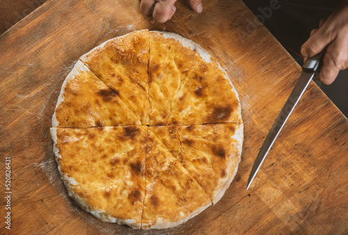 Person cutting  homemade cheese pie on wooden background. Bulgarian banitsa, Georgian khachapuri, Greek tiropita photo