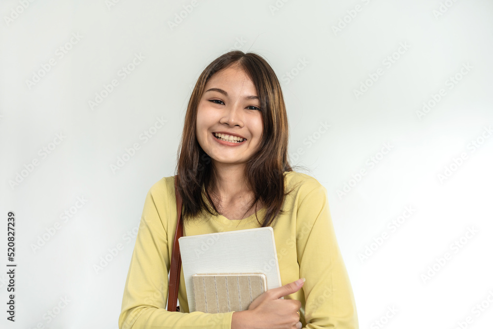 Young woman student is standing and smiling to looking on camera while holding books and bags Young woman student is standing and smiling to looking on camera while holding books and bags