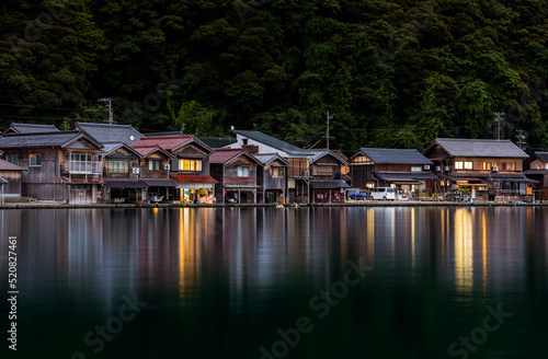 Fotografiet Traditional wooden boathouses reflect of calm water as night falls on Ine, Kyoto