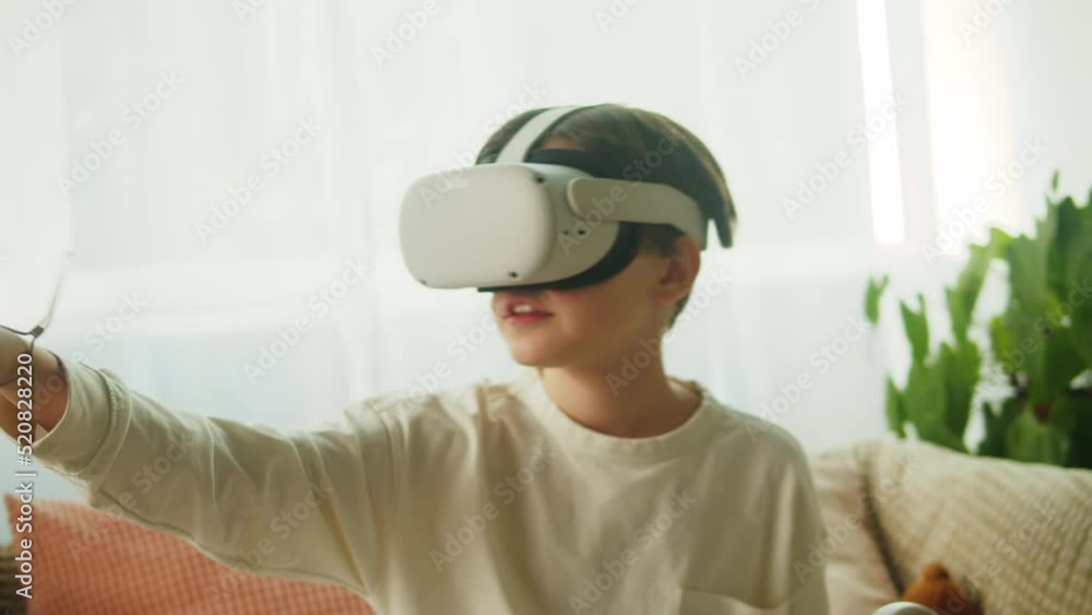 Boy using virtual reality glasses with controllers, playing video games, child gamer wearing new generation gaming headset for entertainment and education at home, future technology concept. Boy using virtual reality glasses with controllers, playing video games, child gamer wearing new generation gaming headset for entertainment and education at home, future technology concept.