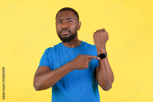 Discontented African American Man Showing Smartwatch Over Yellow Background