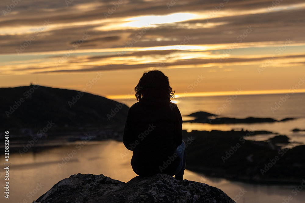 a woman observes midnight sun from Ornfloya Hiking Trail at Sommaroy (Sommarøy), Tromso Norway a woman observes midnight sun from Ornfloya Hiking Trail at Sommaroy (Sommarøy), Tromso Norway