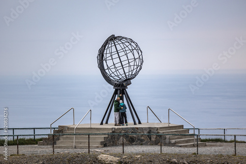 tourists to North Cape (Nordkapp), on the northern coast of the island of Mageroya in Finnmark, Northern Norway. Globe that marks the northern point of Europe in a cloudy day