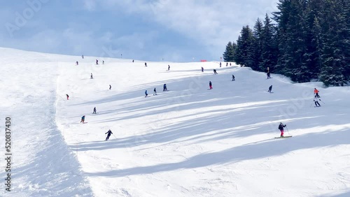 Skiers on alpine ski resort go down the slope view from above
