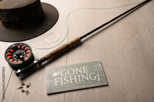 Gone fishing sign, and fly fishing tackle, on a light wood background