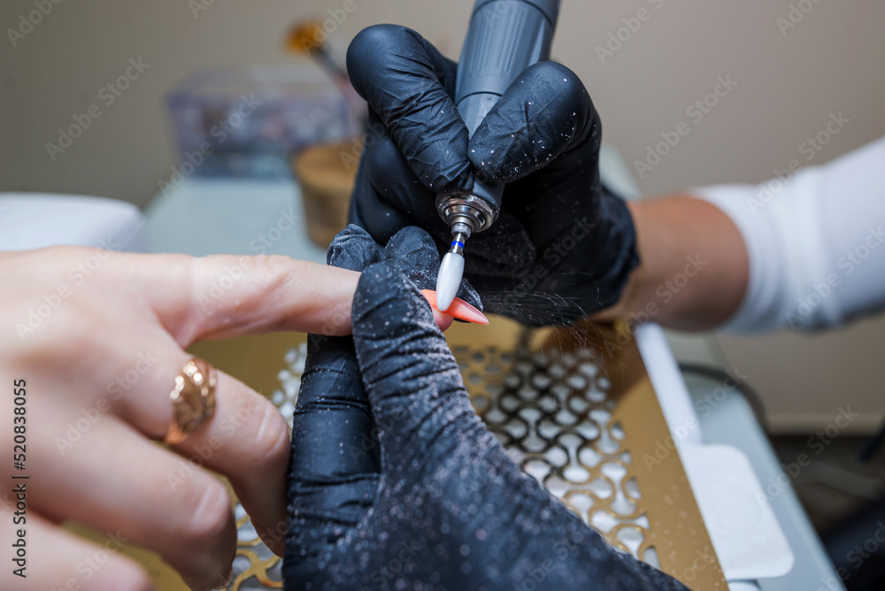 Close-up of a woman in a nail salon getting a manicure in a beauty salon from a beautician who uses an electric nail polish remover machine with flying shards all around.