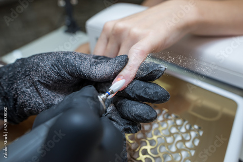 Close-up of a woman in a nail salon getting a manicure in a beauty salon from a beautician who uses an electric nail polish remover machine with flying shards all around. © Tania