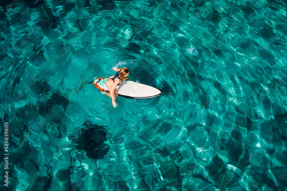 Surf girl sit on surfboard and wait wave in turquoise ocean. Aerial view with surfer woman